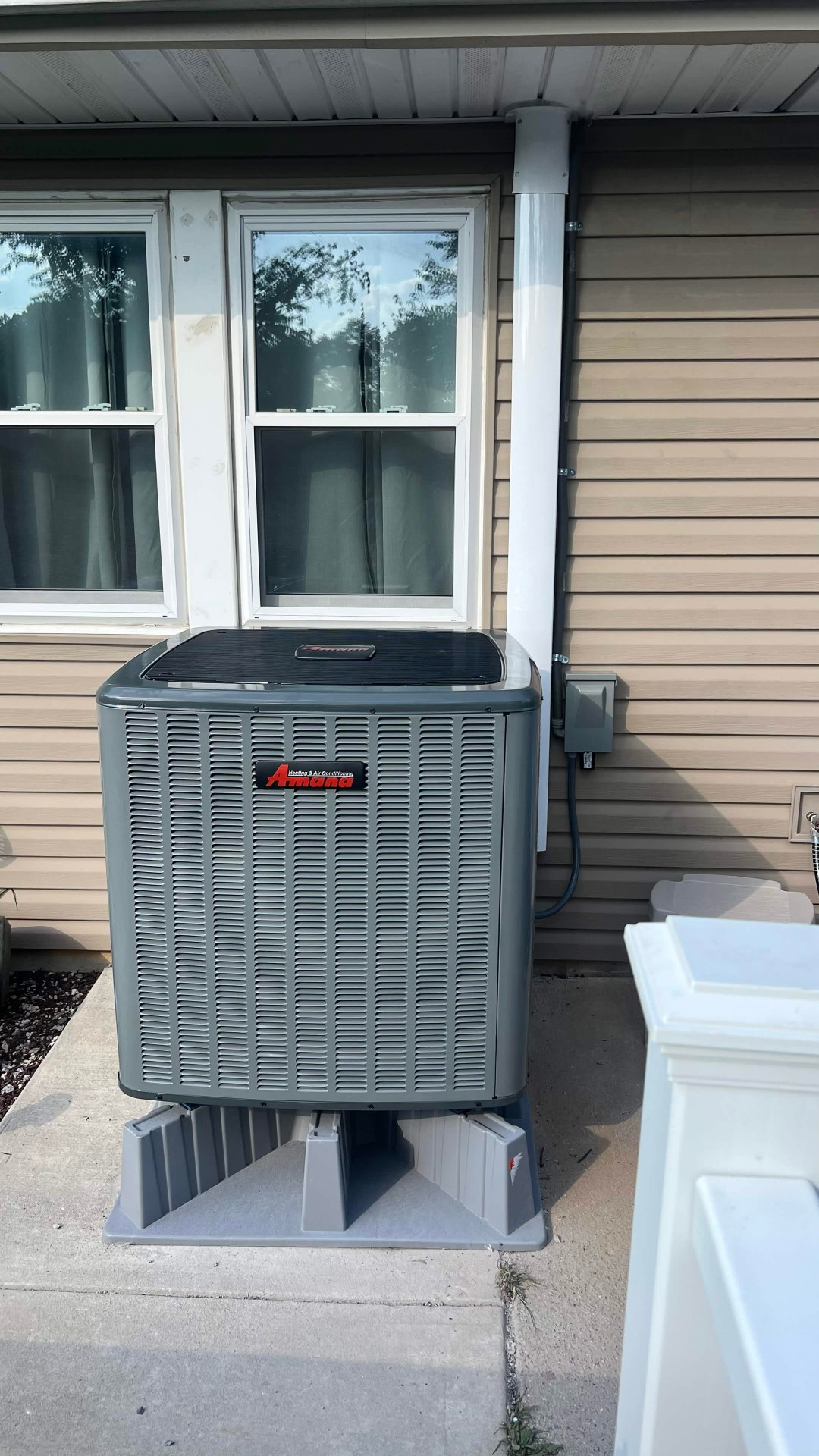 Exterior Amana condenser installed on a raised pad by C&S Heating & Cooling.
